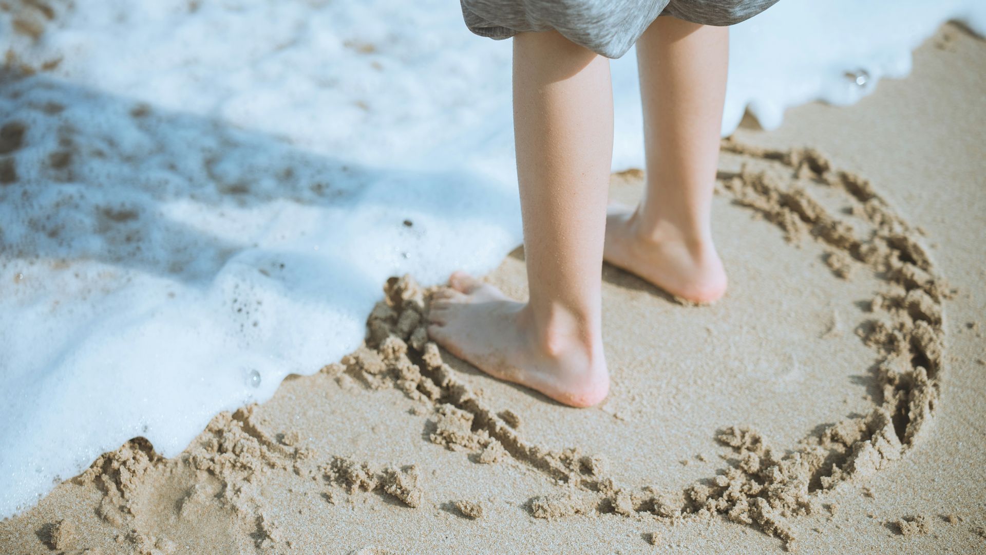 Un enfant pieds nus au bord de l'eau, un cercle dessiné dans le sable